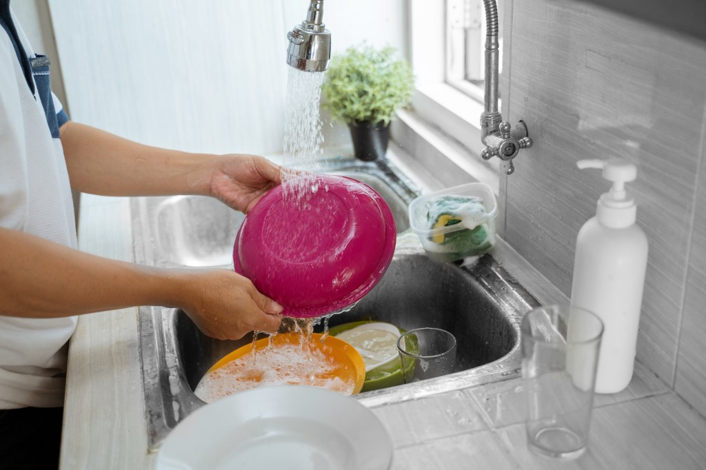 A close-up of a person's hand rinsing a dish in a kitchen sink