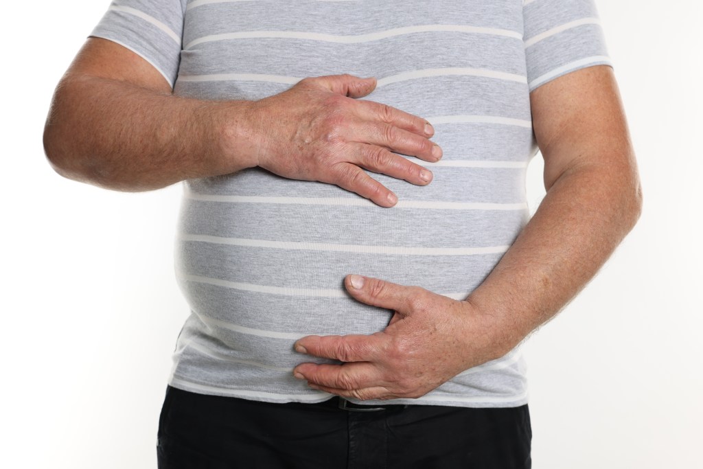 Close up of an overweight man in a tight t-shirt holding his stomach, isolated on white background