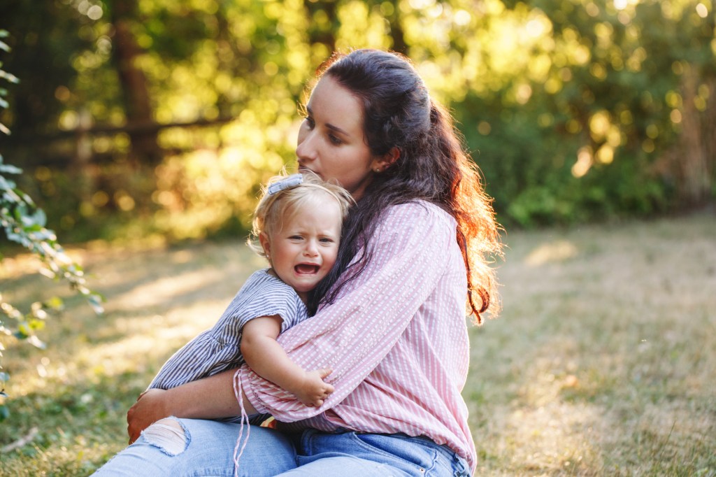 A young mother comforting her upset and crying little daughter in an outdoor park