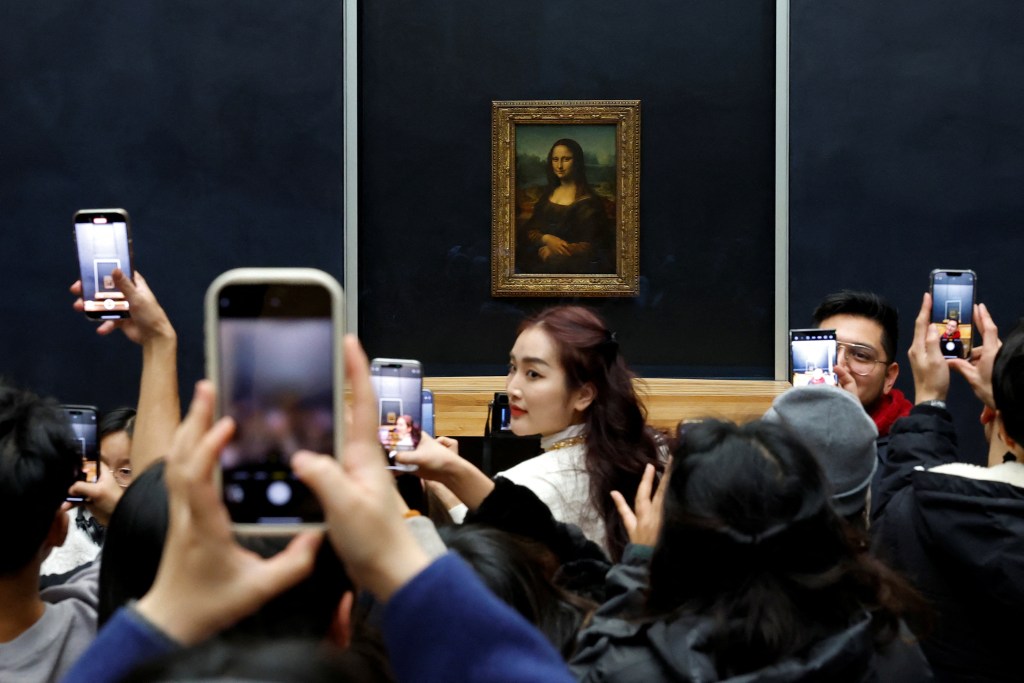 Visitors photographing the Mona Lisa painting by Leonardo da Vinci at Louvre Museum in Paris, France