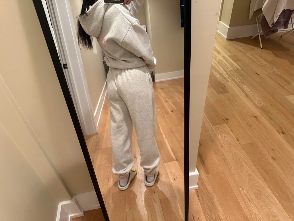 Young woman taking a selfie in a mirror, wearing a gray keyboard with pink bows and smiling face slippers