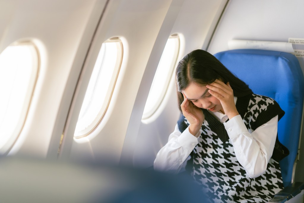 Asian woman sitting on a plane feeling sleepy and having headaches